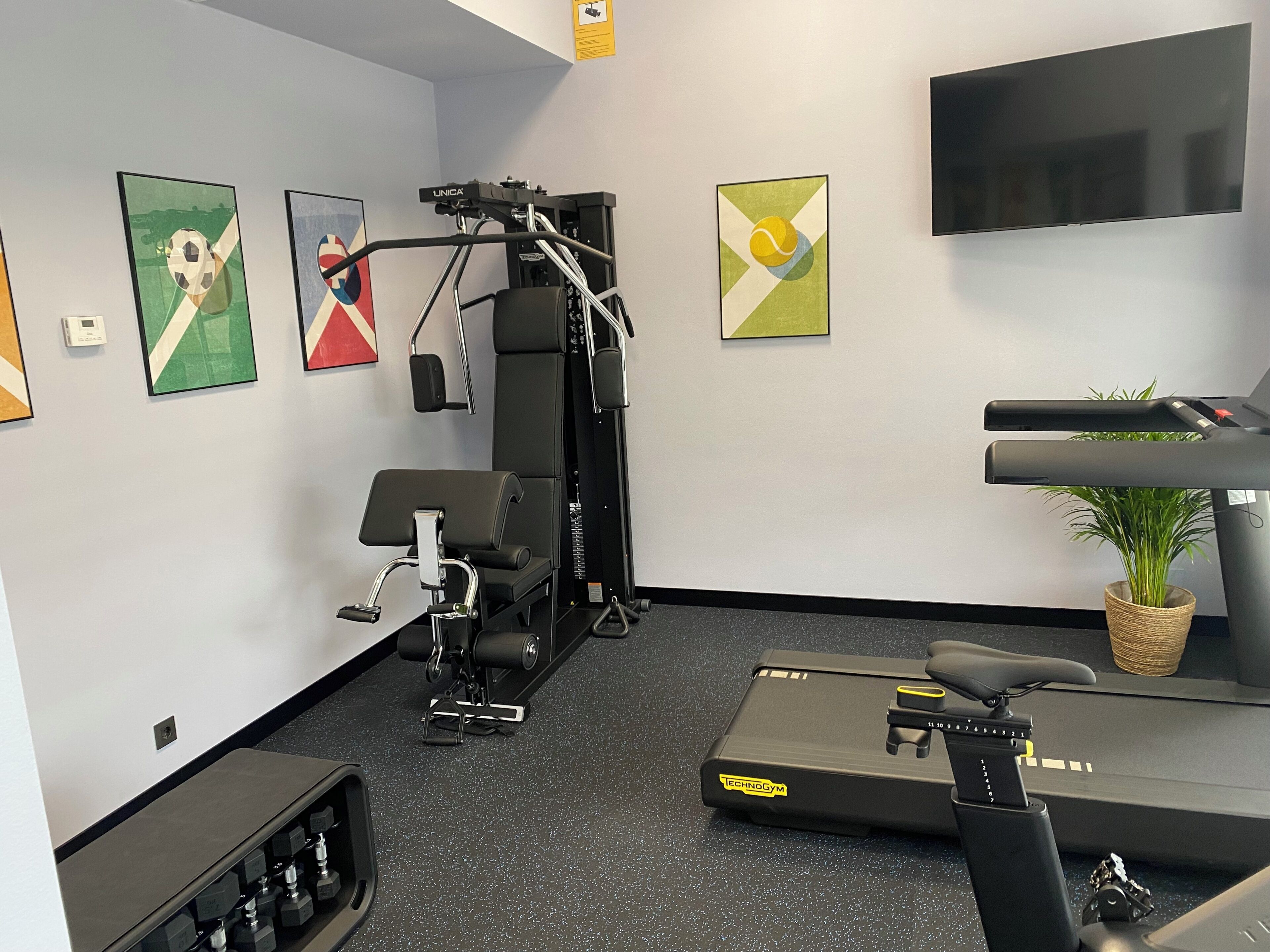 A gym with exercise equipment, a treadmill, and a TV on the wall.