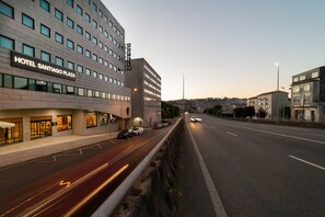 Ein modernes Hotel mit einem Schild, auf dem „HOTEL SANTIAGO PLAZA“ steht, und einem mehrstöckigen Gebäude mit schlichter Fassade und zahlreichen Fenstern.