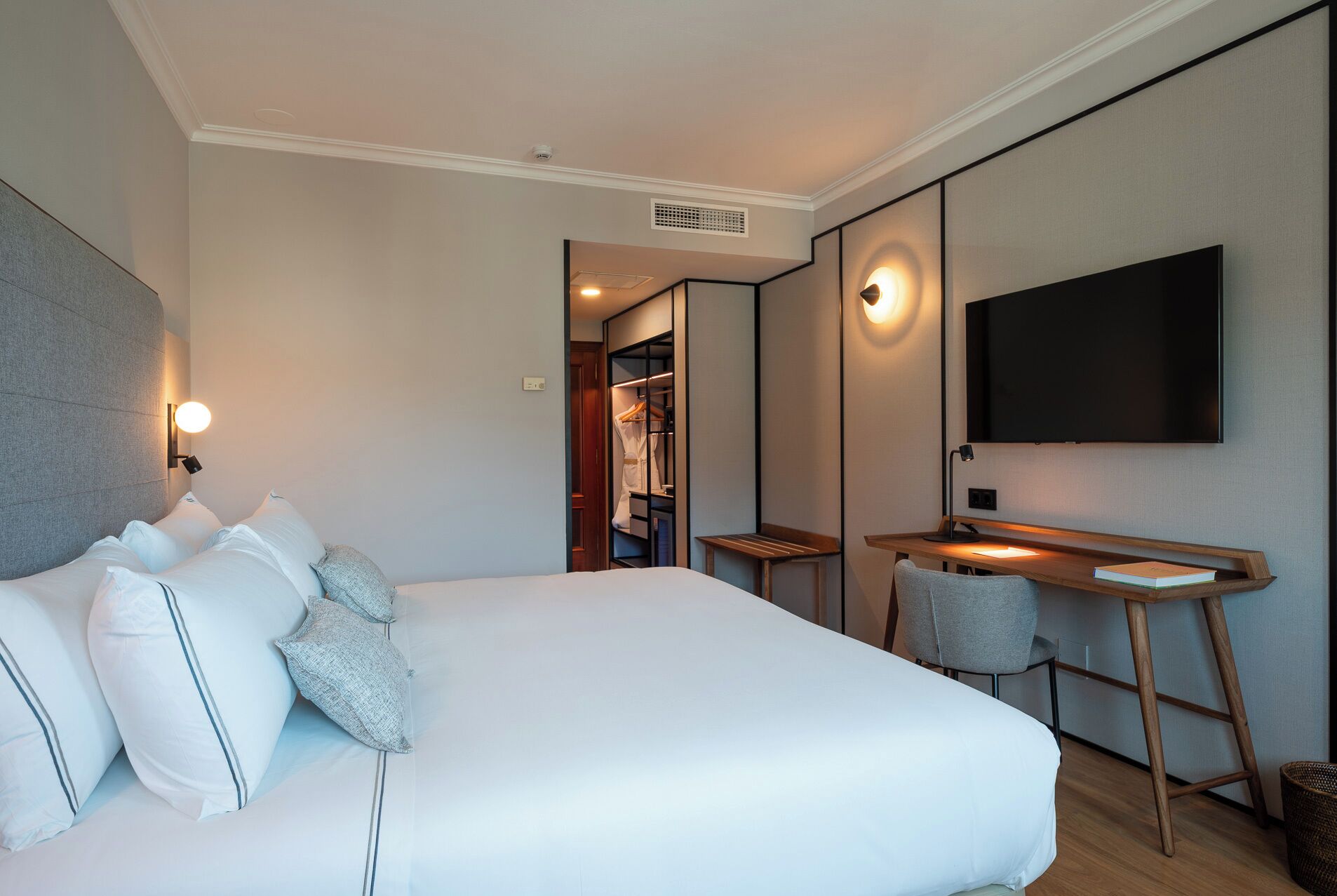 Ein Hotelzimmer mit Bett, Schreibtisch, Sessel, Fernseher und Kleiderschrank.