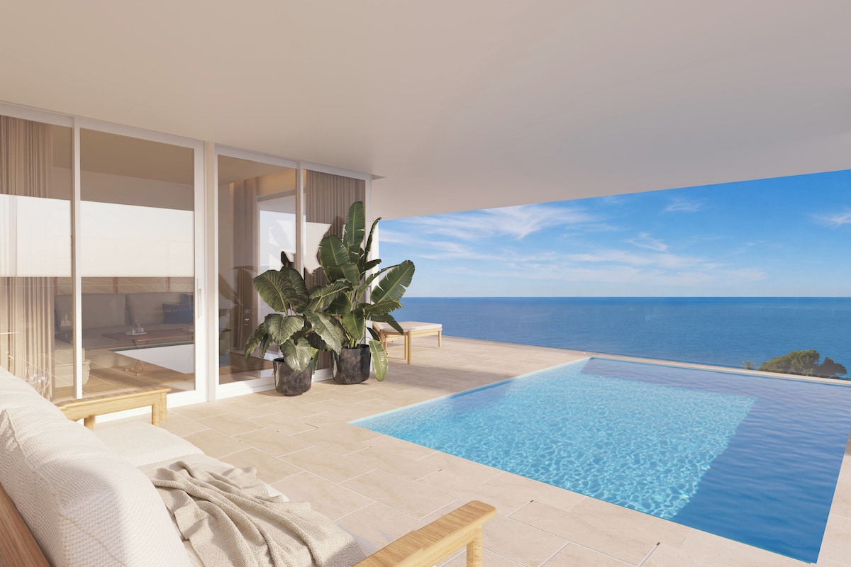 Una piscina infinita moderna con vista despejada al océano, un área de descanso confortable con un sofá y un banco, y plantas grandes en macetas.
