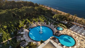Un resort con una piscina grande central, una piscina más pequeña y una zona de playa.