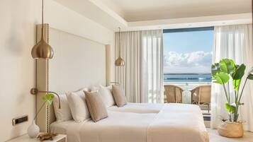 Habitación de hotel con una cama grande, una mesita de noche con lámpara, vista al océano y un balcón con una silla.