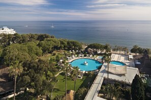 Un resort con una amplia piscina central, palmeras y vista al mar.