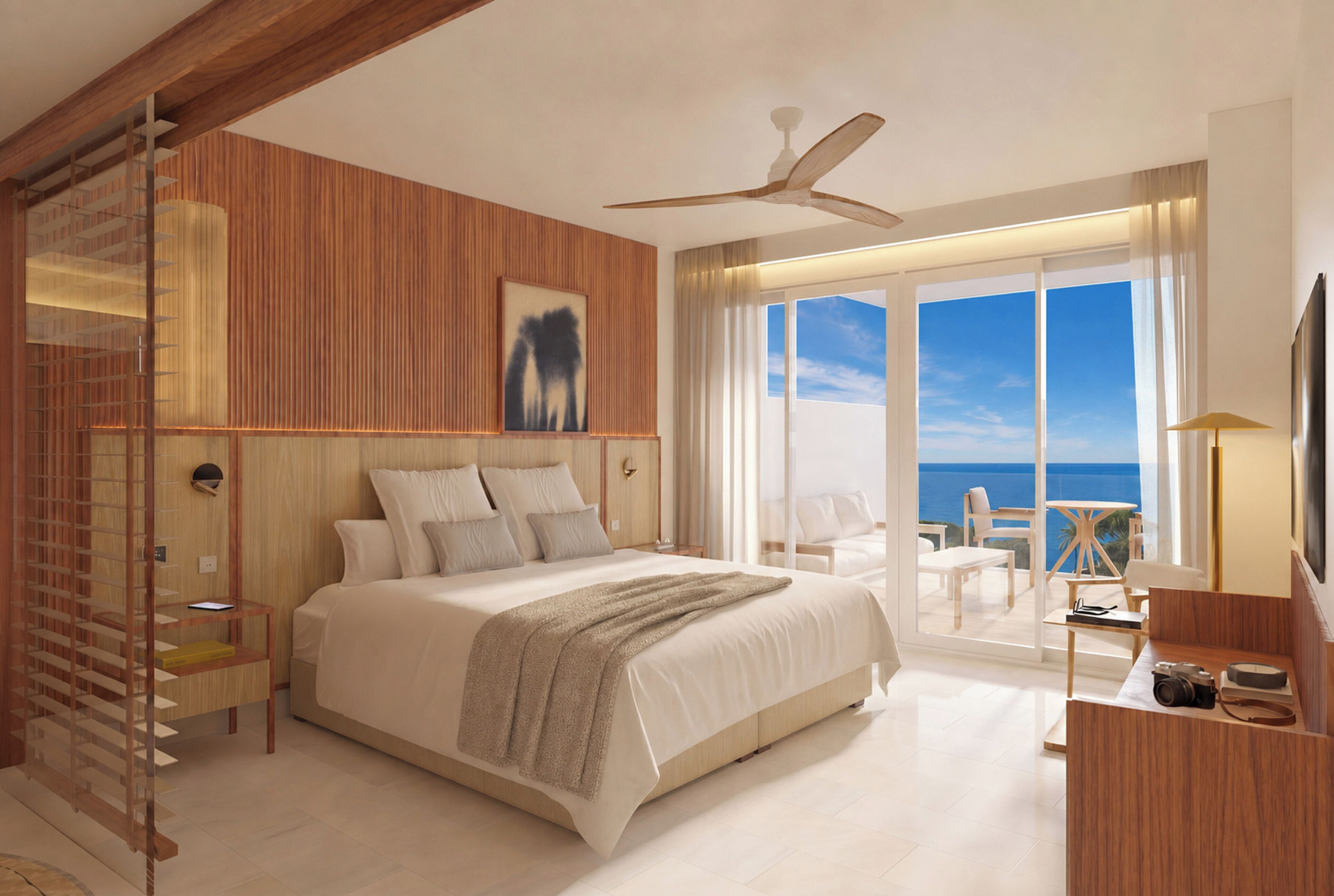 A modern bedroom with a large bed, a ceiling fan, and a view of the ocean.