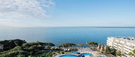A resort with a large swimming pool, lush greenery, and a view of the sea.