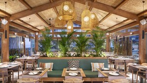 Un restaurante con mesas y sillas de madera, un sofá verde y lámparas colgantes de mimbre.