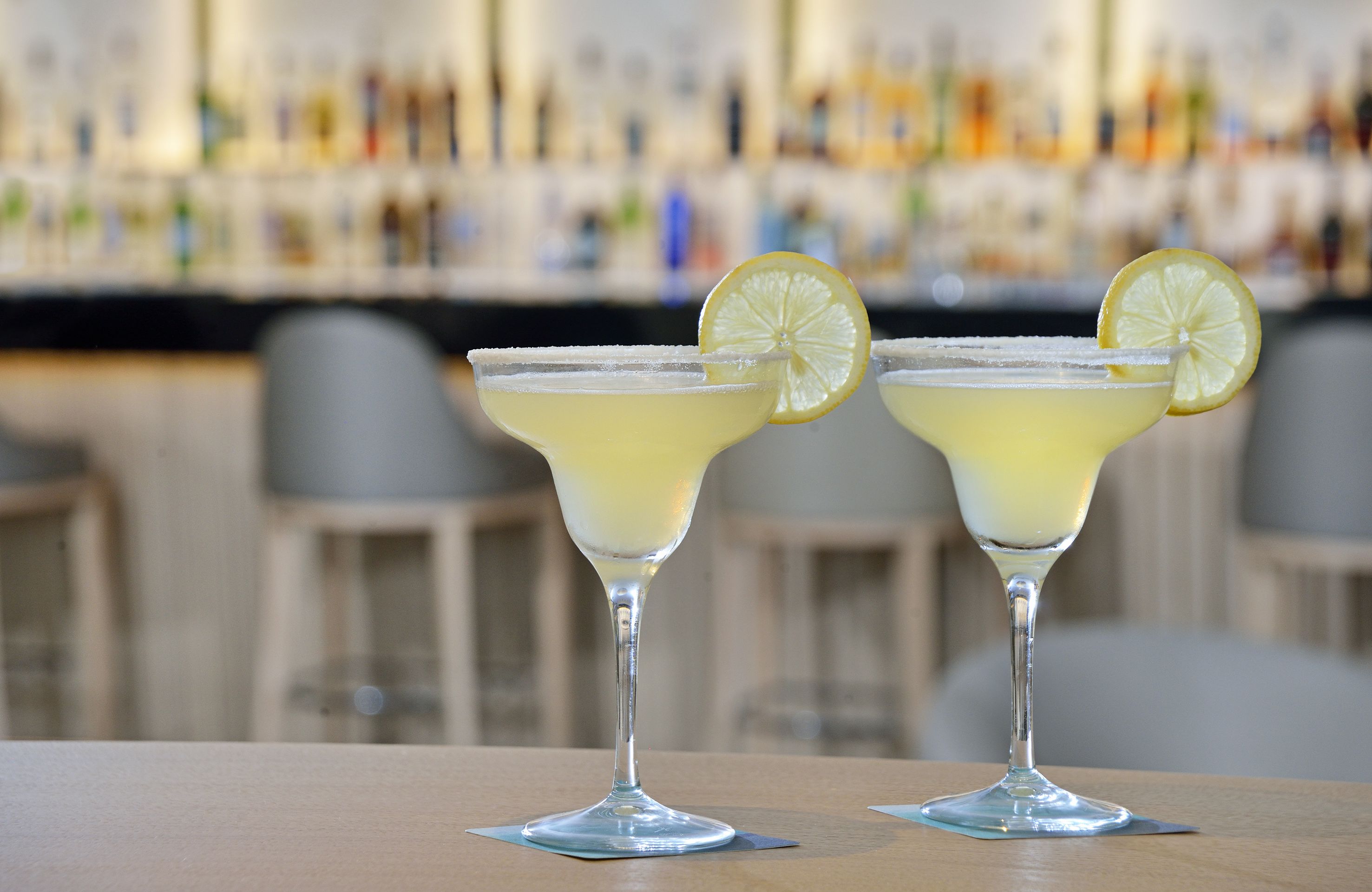 Dos margaritas con rodajas de limón sobre una barra.