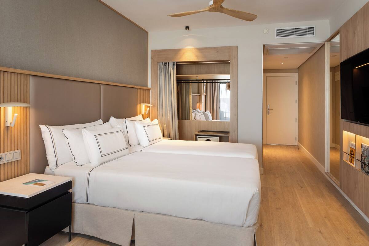 Ett modernt hotellrum med en stor säng, sängbord, en takfläkt och en tv.