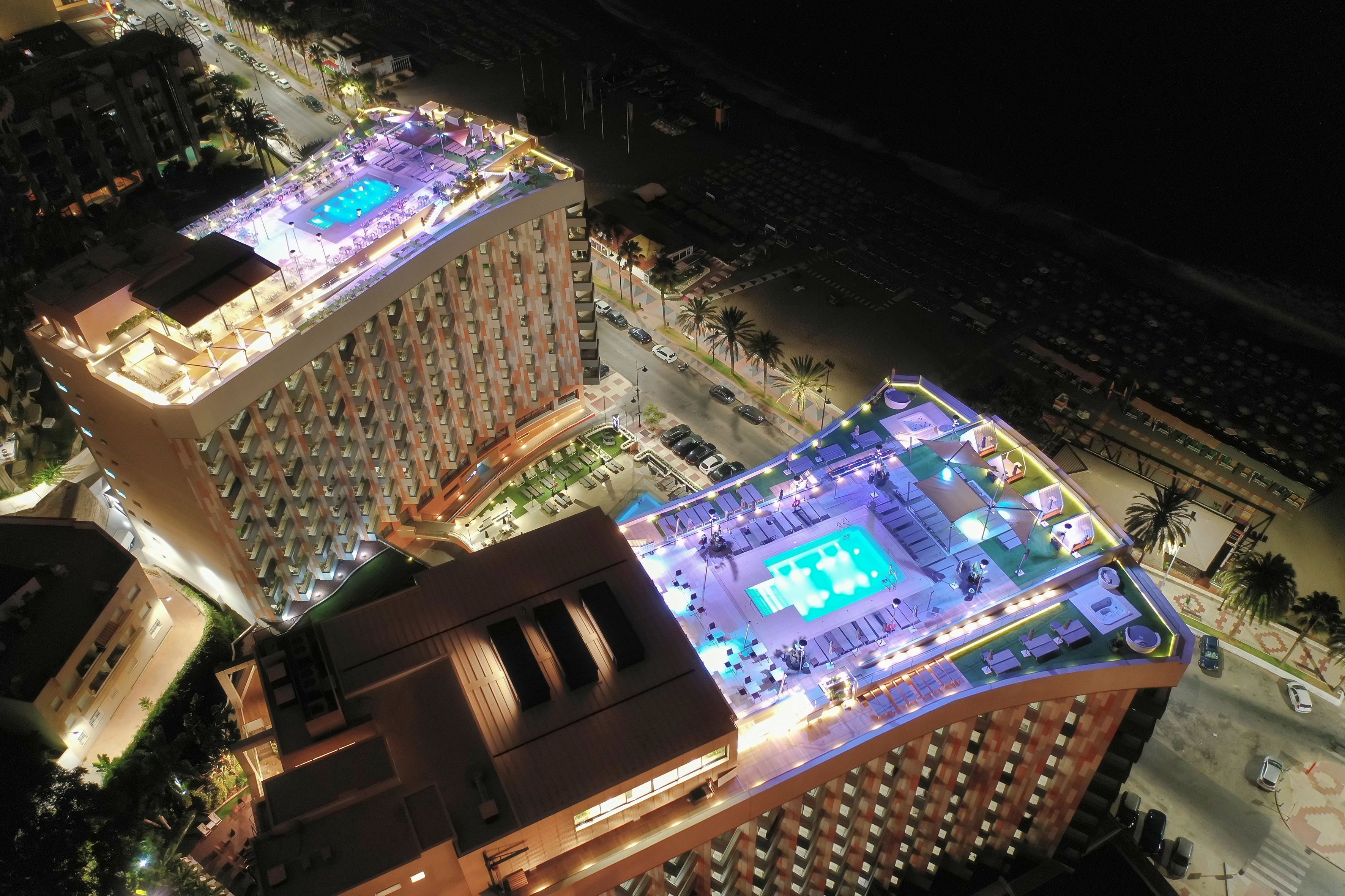 A high-rise hotel with multiple balconies, a rooftop pool area, and a well-lit street view.