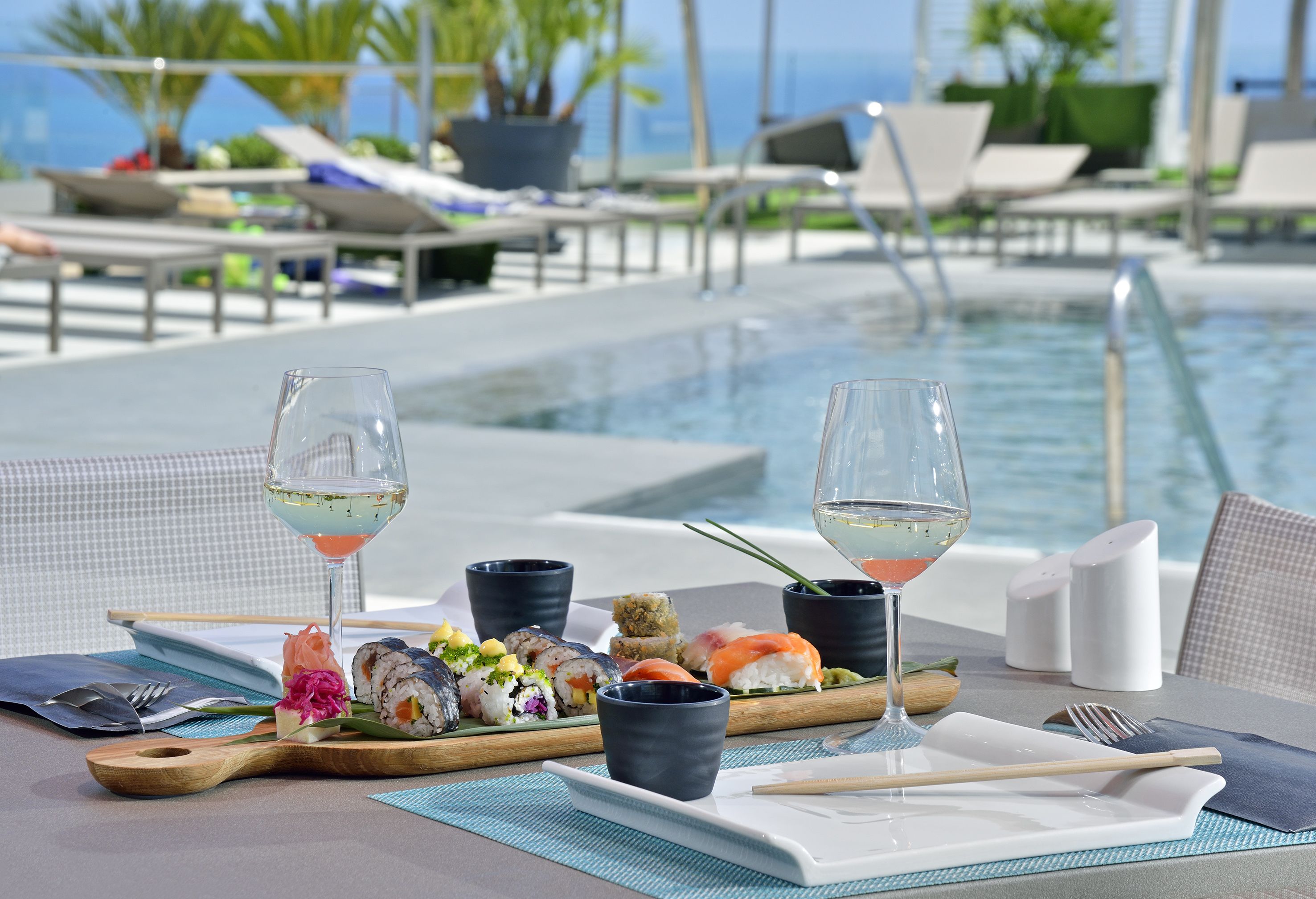 Ein Esstisch mit Sushi, Weingläsern und Blick auf Pool und Meer.