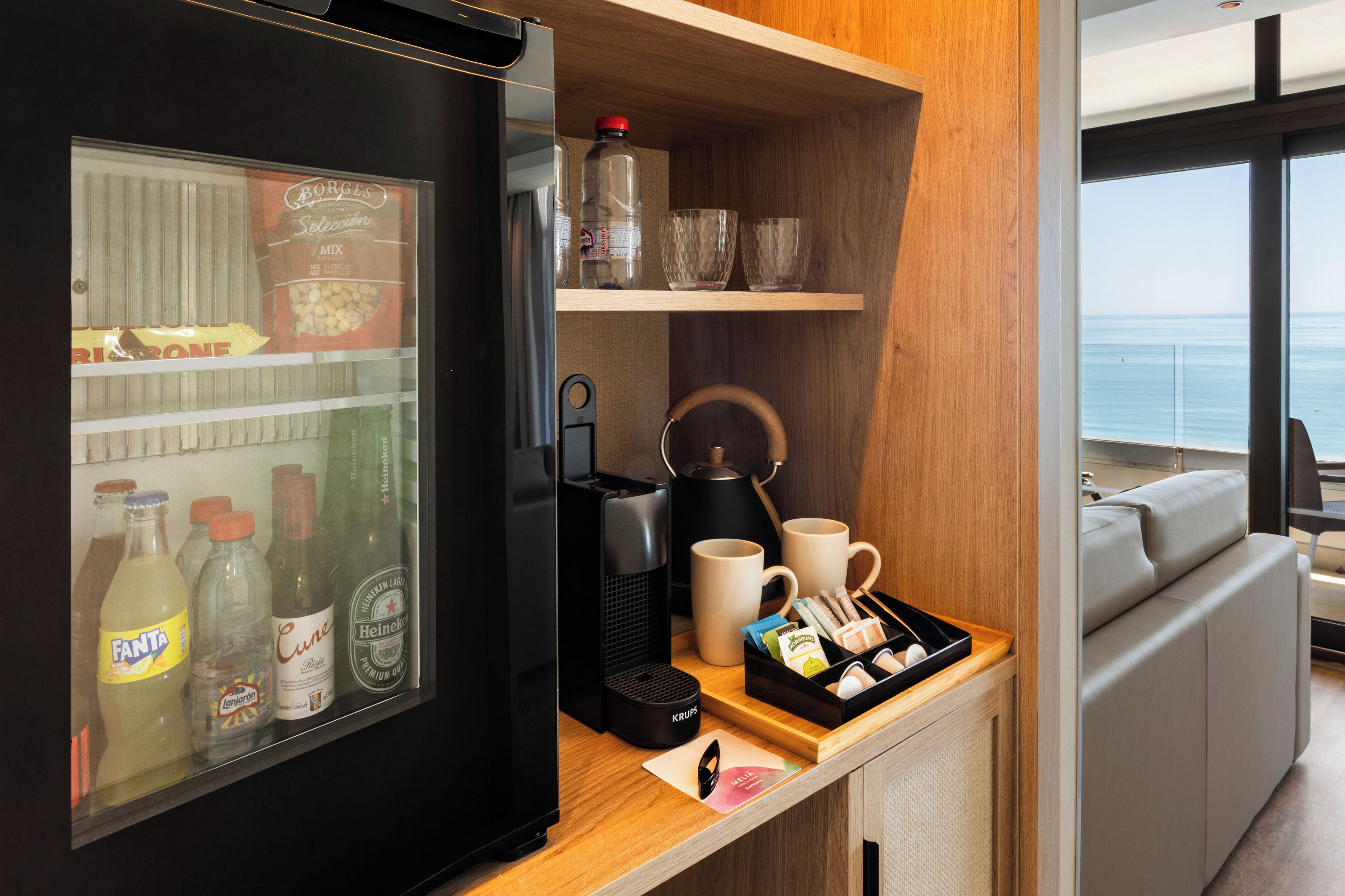 Een keuken met een koelkast, koffiezetapparaat en waterkoker. Ook zijn er bekers, een schaal met snacks en uitzicht op de oceaan.