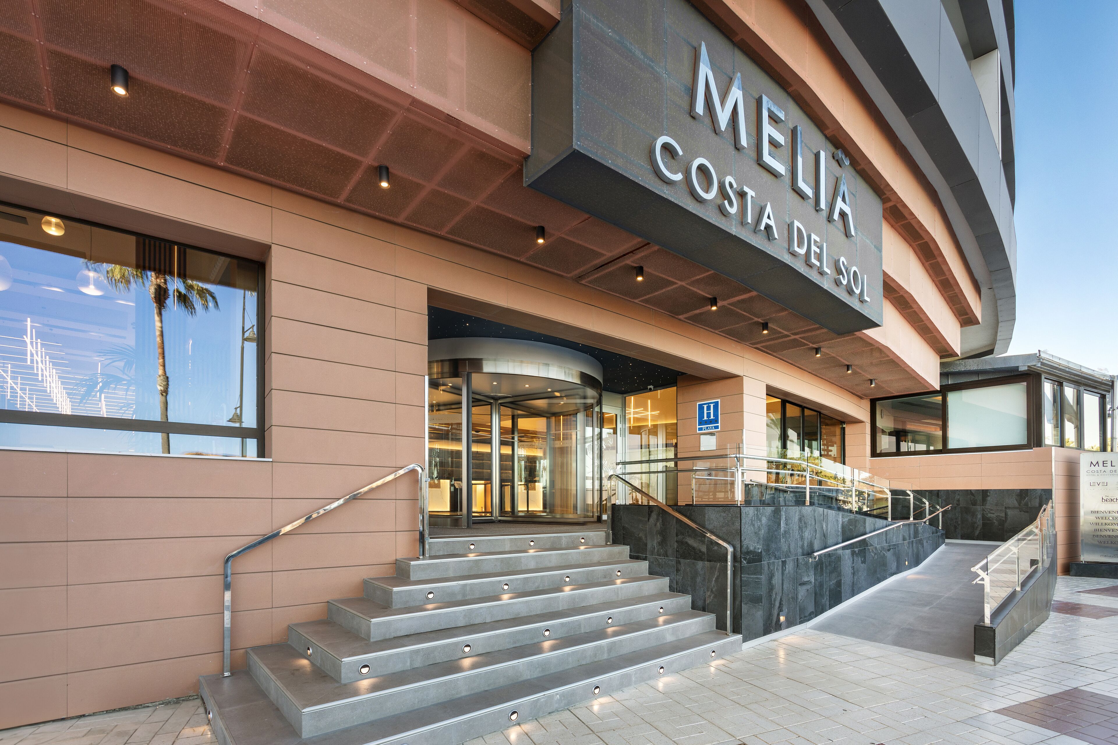 A hotel entrance with a curved facade, a staircase, and a glass door leading inside.