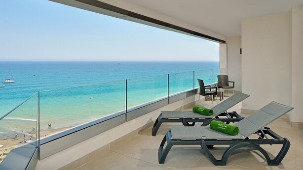 Un balcón con dos sillones de relax y una mesa, con vistas a una playa y al mar.