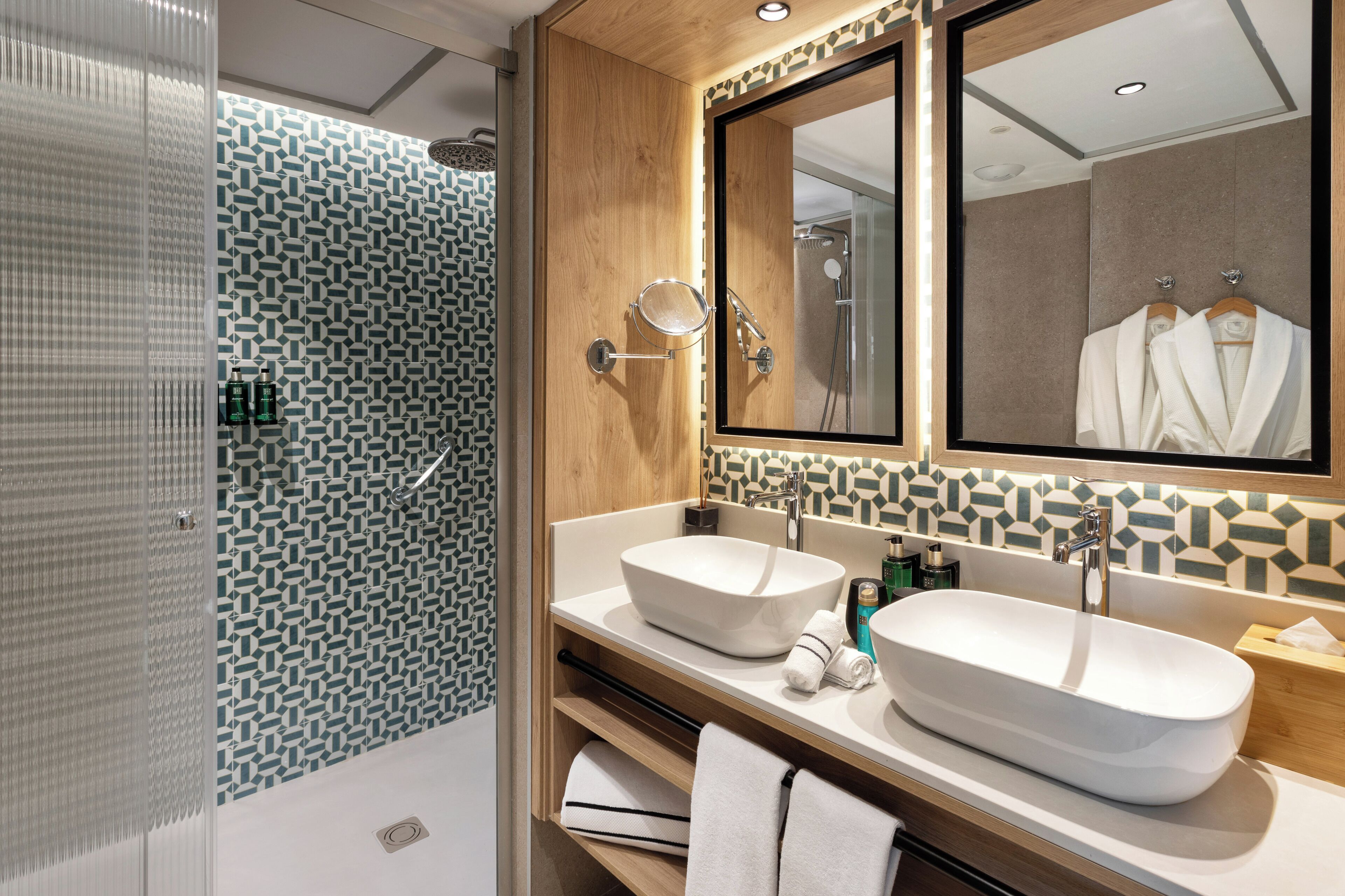 Un baño moderno con un espejo grande, dos lavamanos y una zona de ducha.