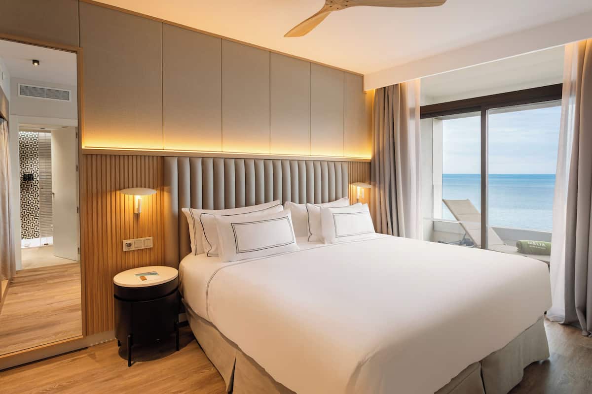 Ett modernt hotellrum med en stor säng, en takfläkt, utsikt över havet och ett badrum med dusch och toalett.