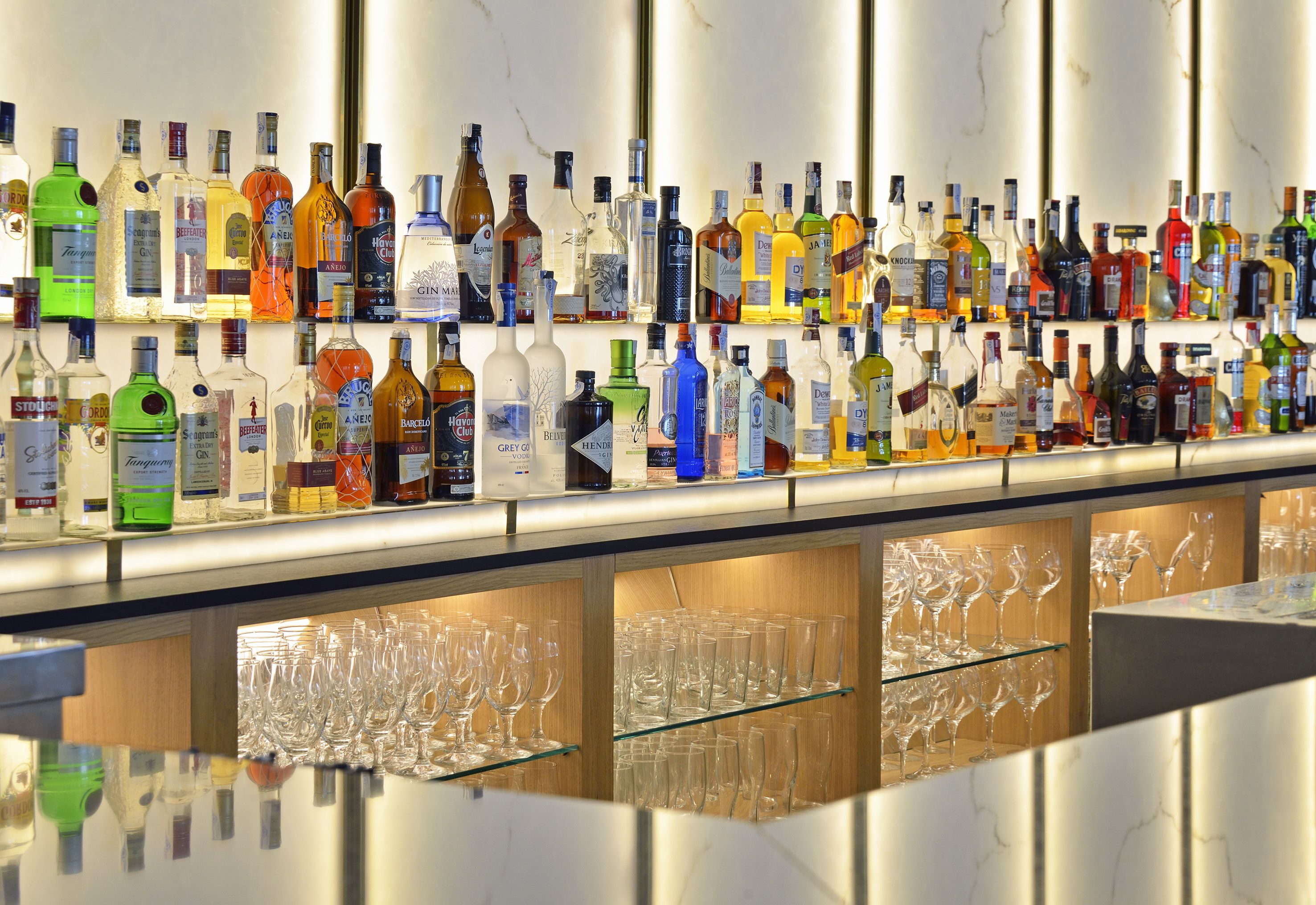 Zona de bar con diversas botellas de licor y numerosos vasos de vino vacíos.