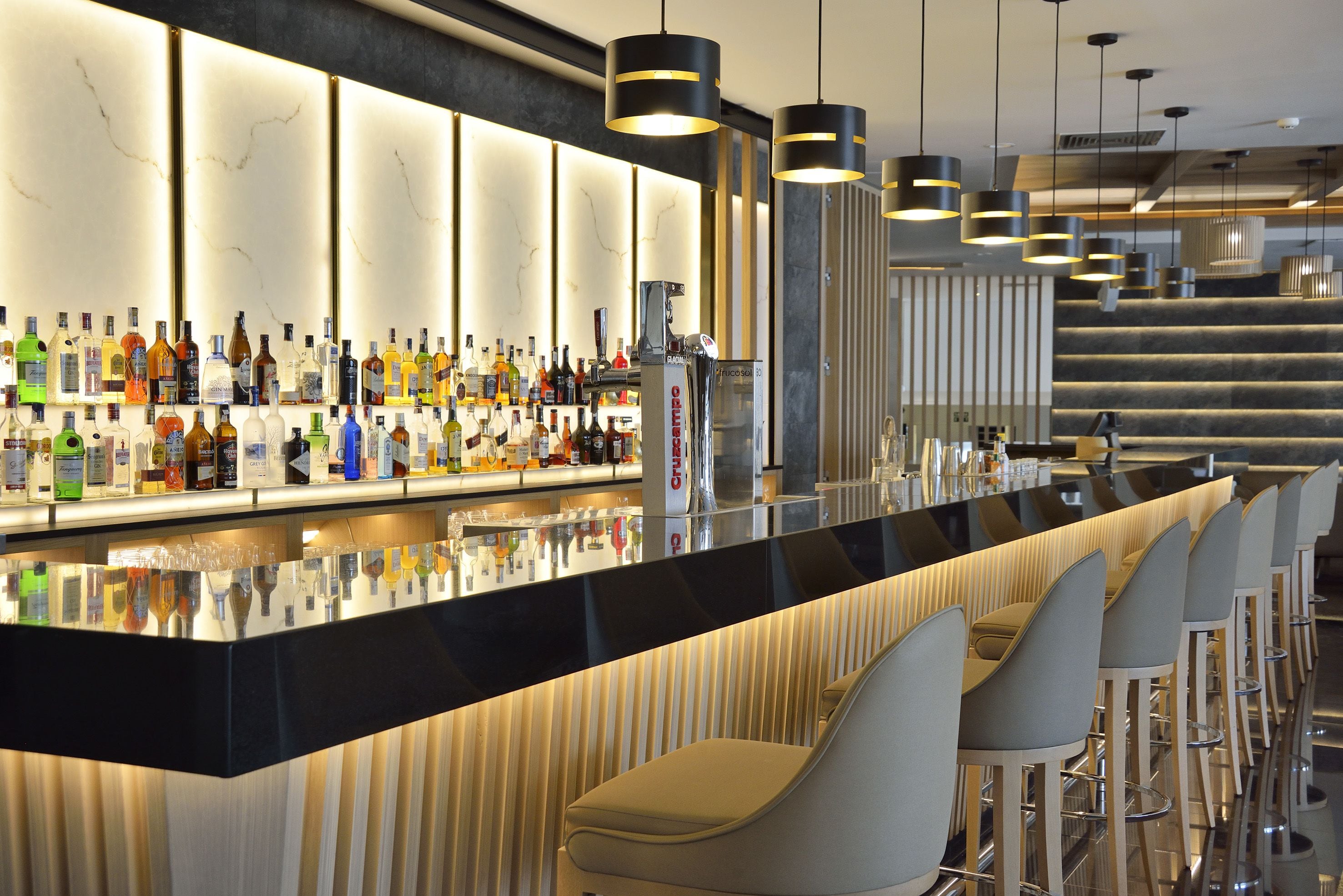 Una zona de bar con una barra larga, varios taburetes y una amplia selección de botellas.