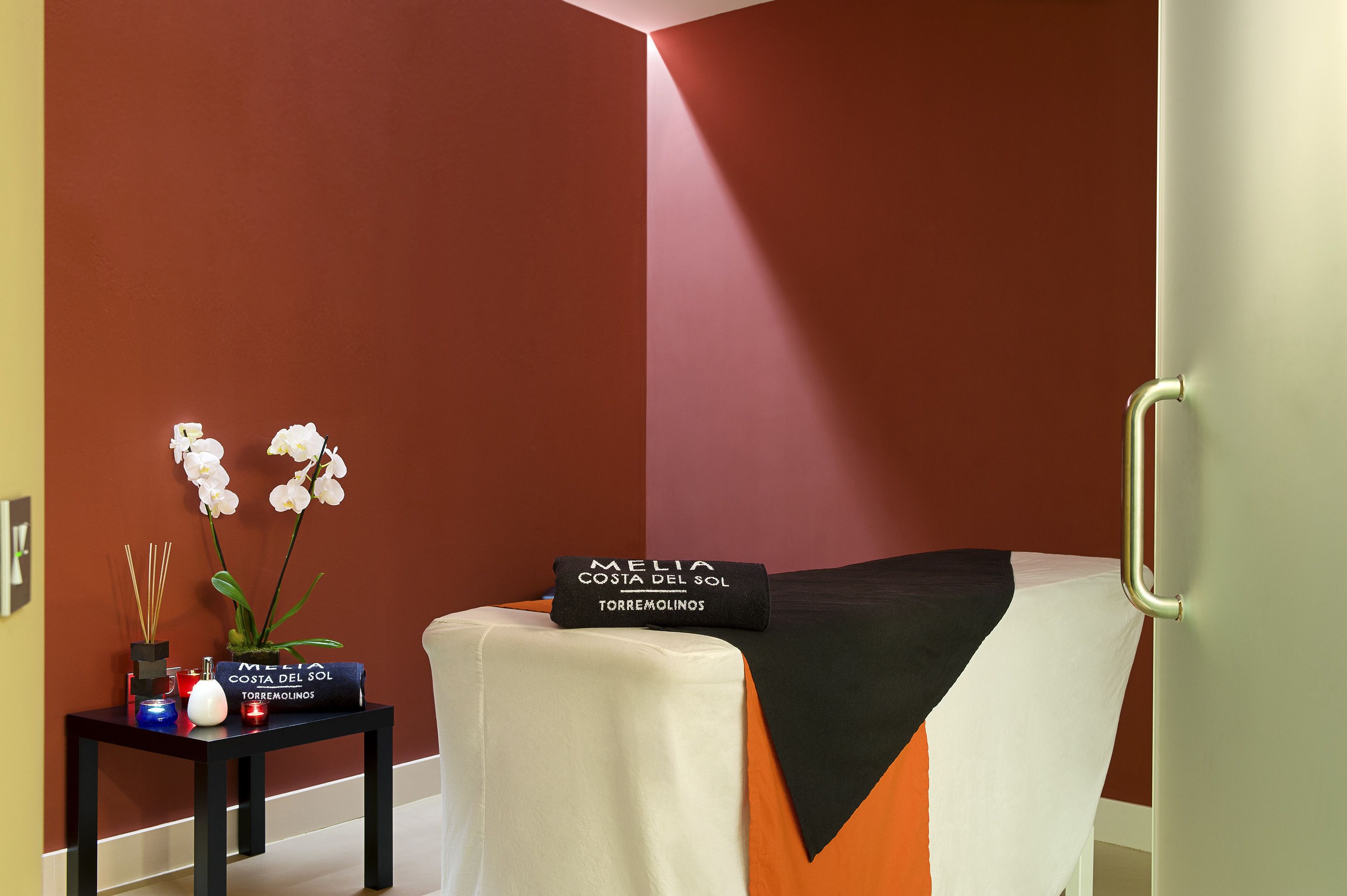 Una habitación ordenada con una cama, una mesita con adornos y una pared con diseño geométrico.