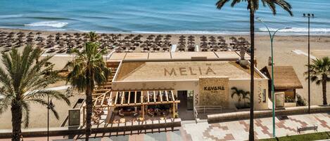 A beachside hotel named 'MELIA' with a patio area, lounge chairs, and a view of the ocean.