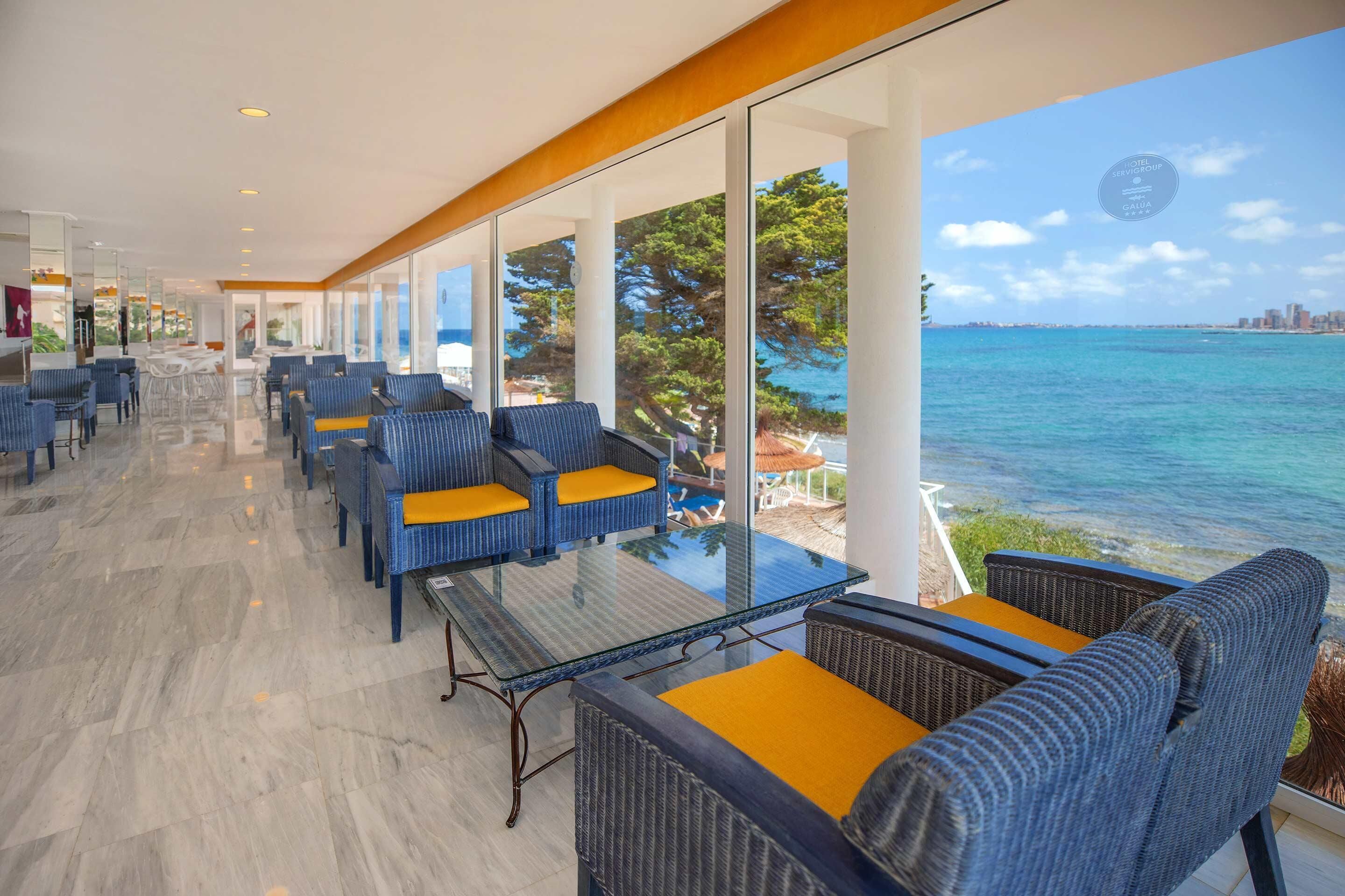 A spacious indoor area with a glass wall offering a view of the sea and a city skyline.
