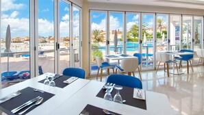 A restaurant with large windows overlooking a pool and a clear sky.