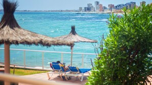 A beachside view with a city skyline in the background, a thatched umbrella, and two lounge chairs with a person using a laptop.