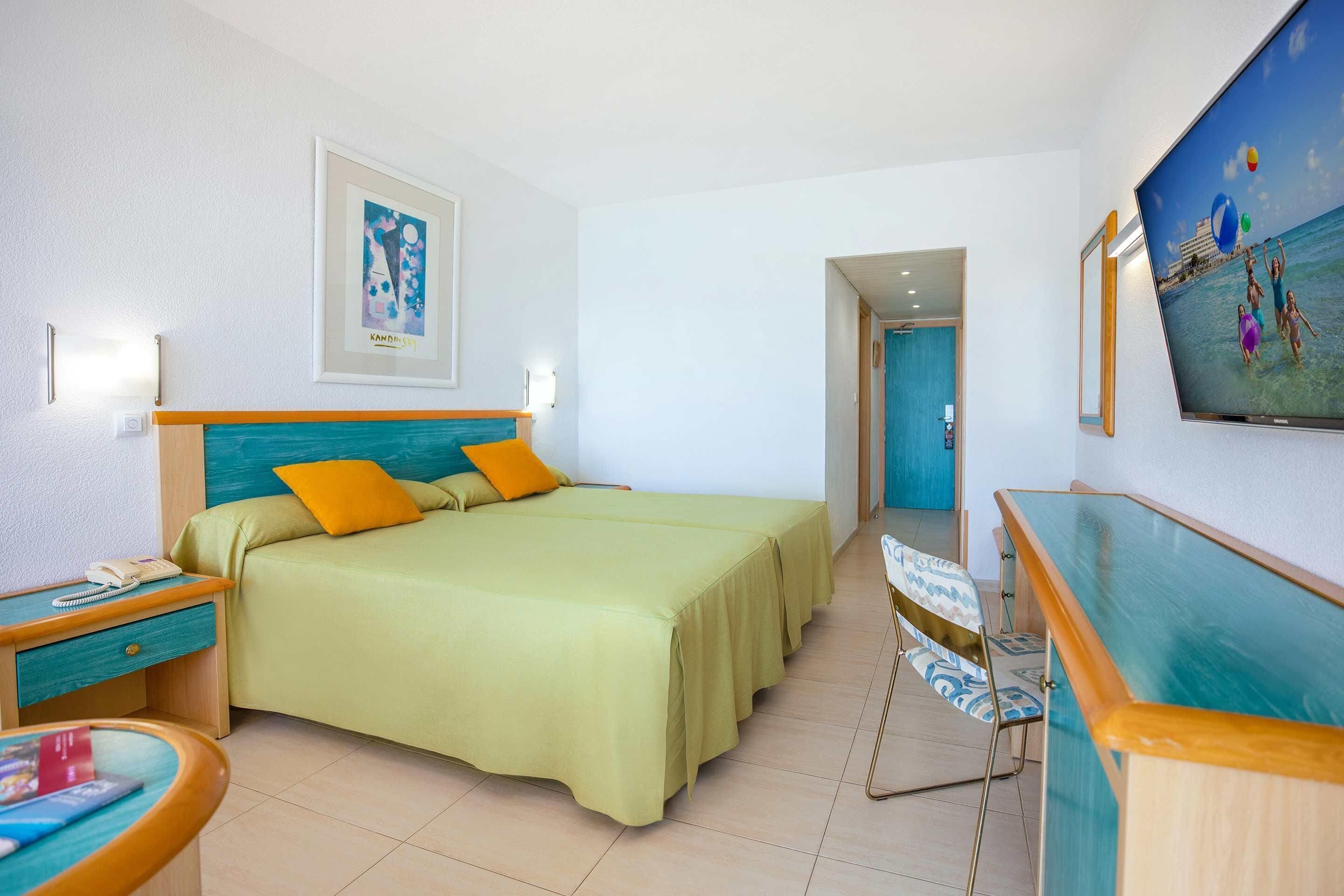 Une chambre d’hôtel équipée d’un lit, d’une table de chevet, d’une chaise, d’un bureau et d’un téléviseur fixé au mur.