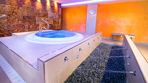 A modern spa area with a hot tub, a stone wall, and a pebble-lined floor.