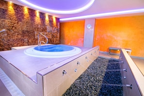 A modern spa area with a hot tub, a stone wall, and a pebble-lined floor. - Hotel Servigroup Galúa (Cartagena)