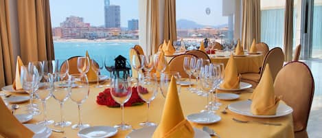 Una mesa de comedor lista para una comida, con vista a la playa y al paisaje urbano.