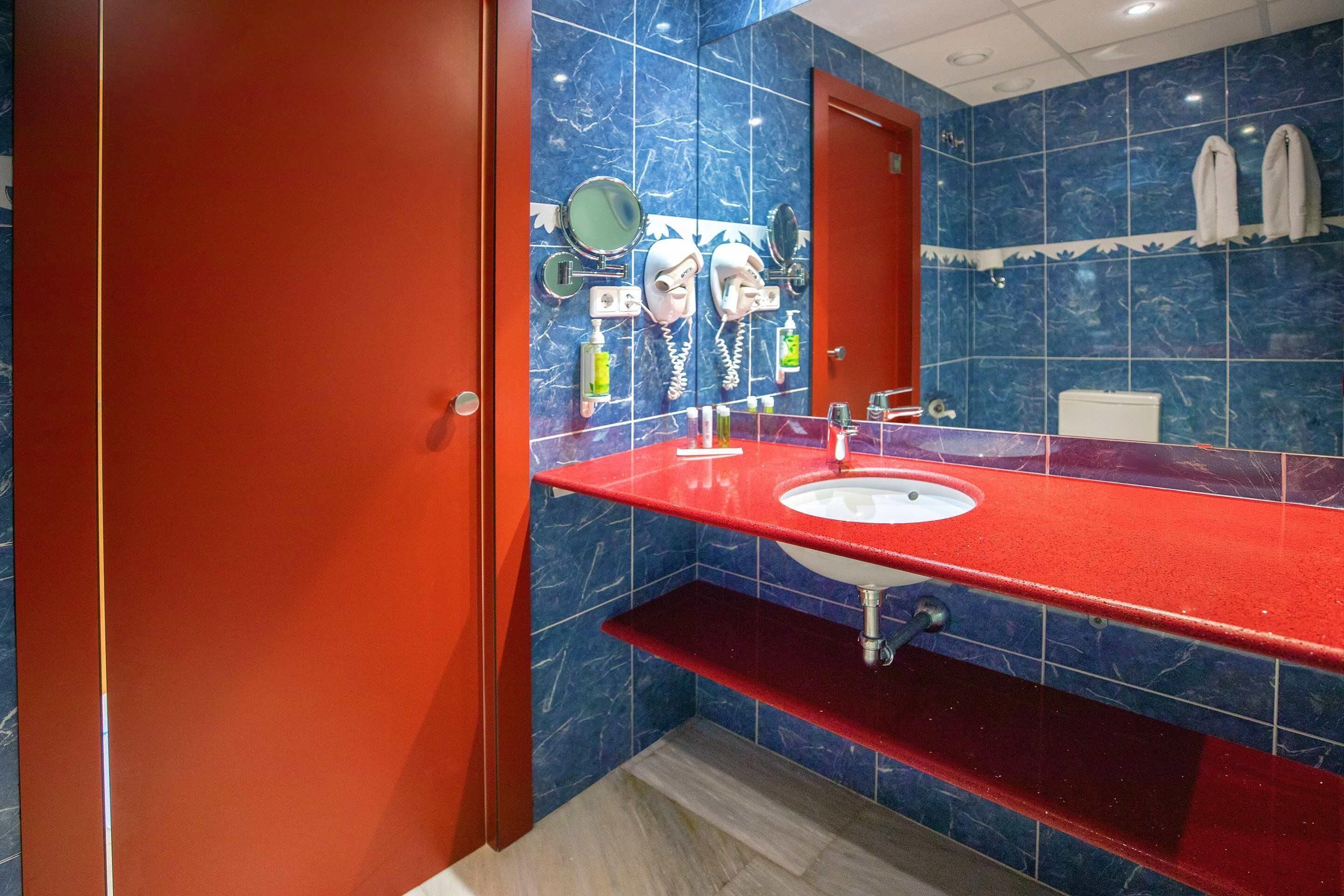 A bathroom with a red sink, blue marble tiles, a mirror, and a toilet.