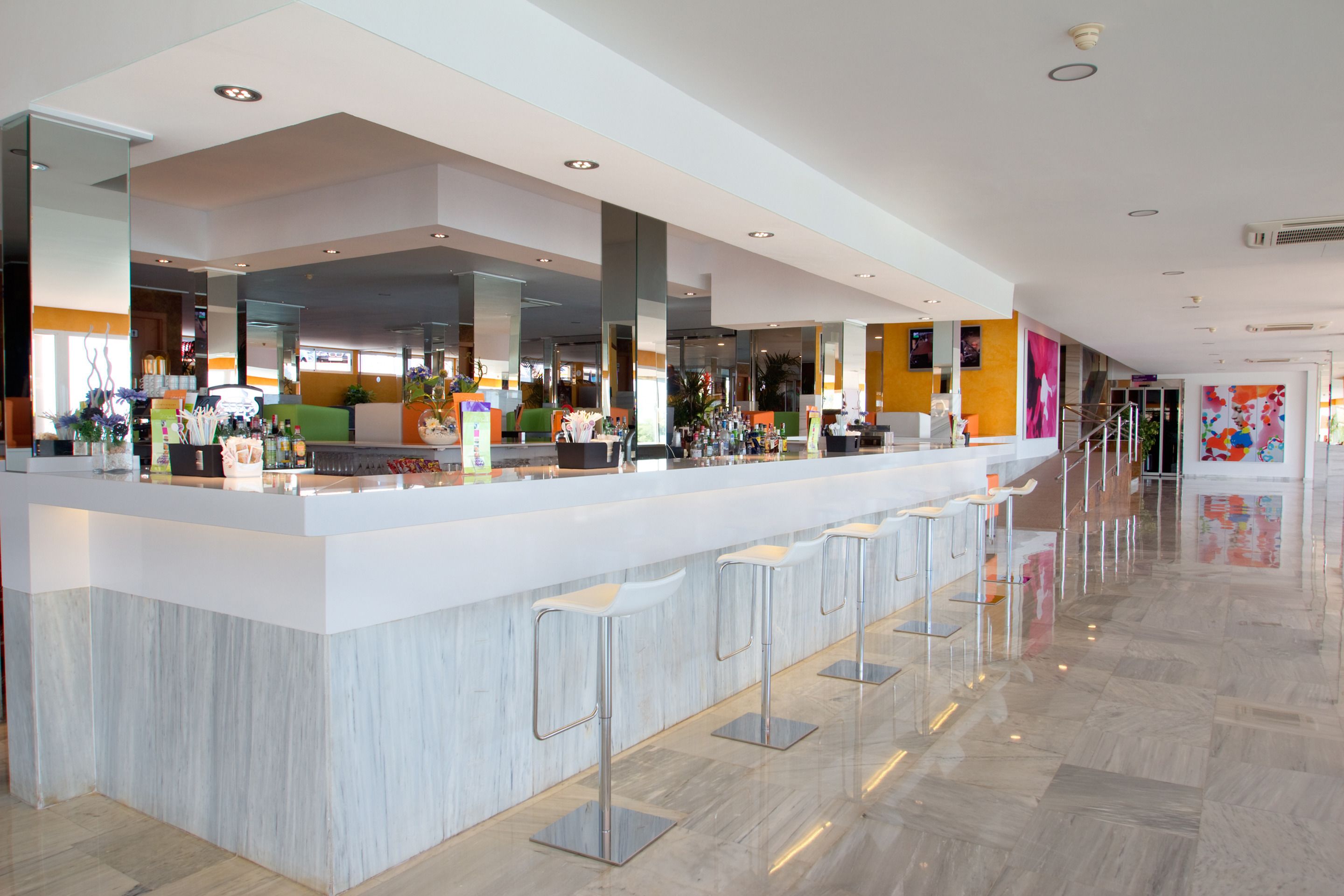 Zona de bar moderna con encimera de mármol, varios taburetes y una variedad de utensilios y botellas de bar.
