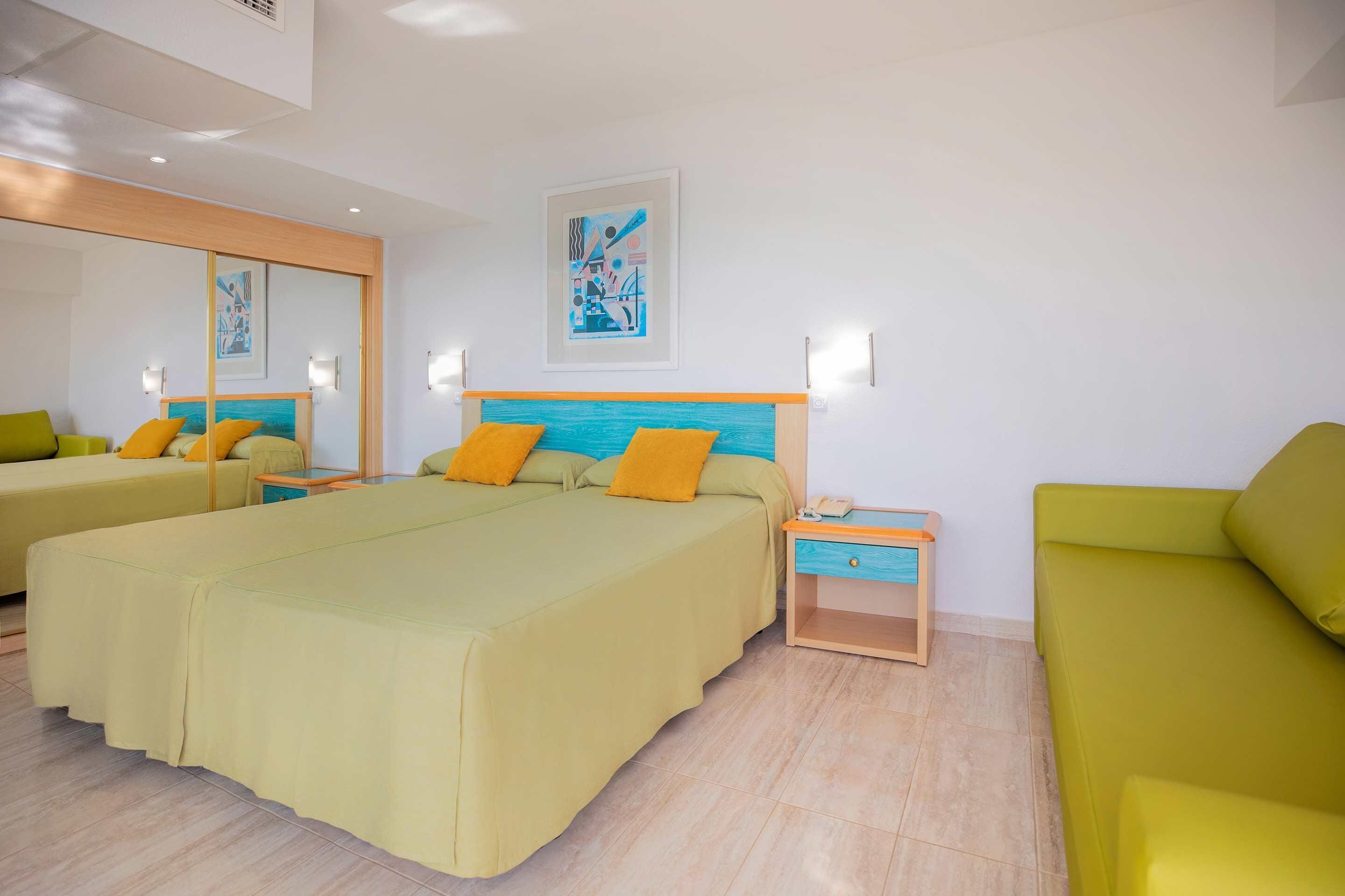 Una habitación de hotel con dos camas, un sofá, una mesita de noche y una obra de arte colgada en la pared.