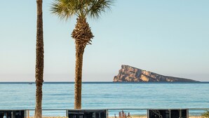 A pool with lounge chairs and palm trees, overlooking a beach and a rocky island. - INNSiDE by Meliá Costablanca - Adults recommended (Benidorm)