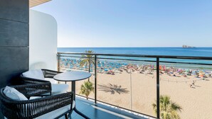 A balcony with wicker furniture, a view of a beach with umbrellas, and a palm tree. - INNSiDE by Meliá Costablanca - Adults recommended (Benidorm)
