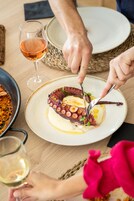 A dining table with a plate of octopus dish, a glass of wine, and a bowl of rice.