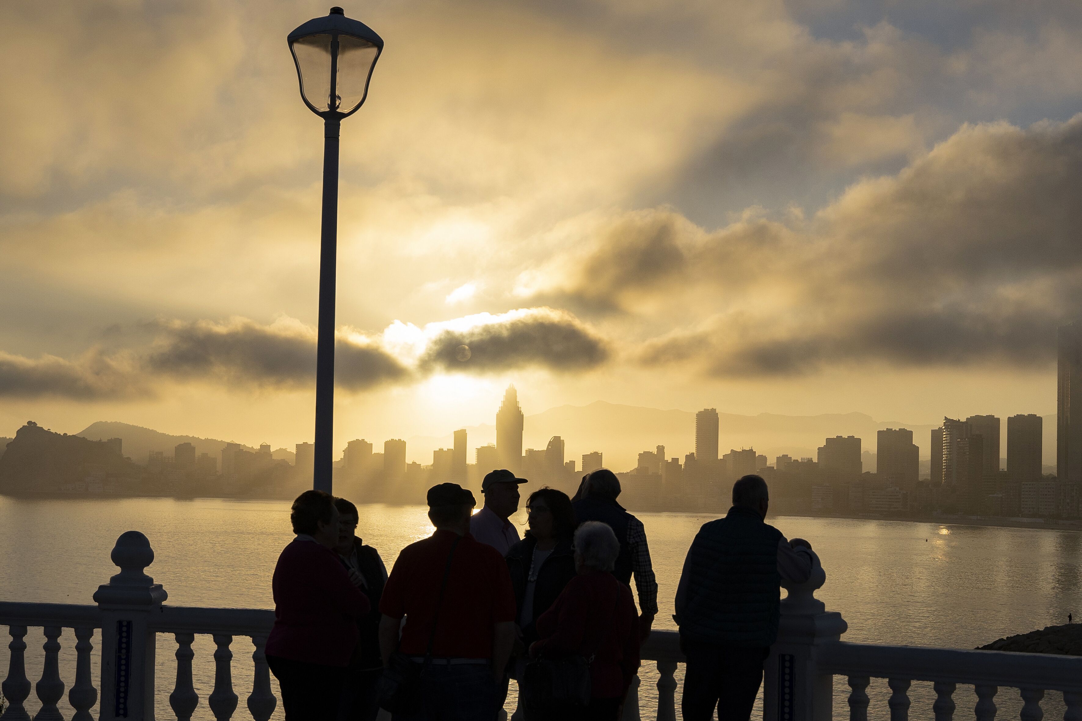 A group of people standing by a waterfront with a city skyline in the background.