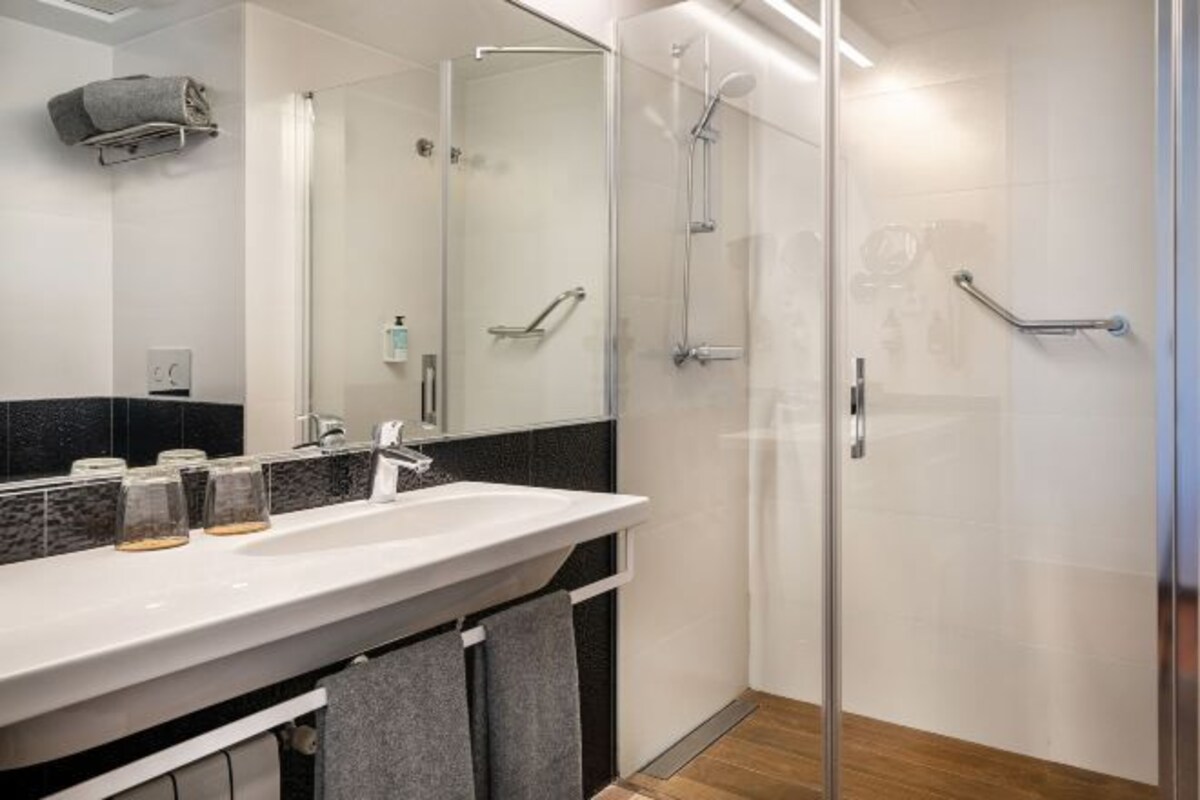 A modern bathroom with a glass shower enclosure, a white sink with a marble countertop, and a towel rack.