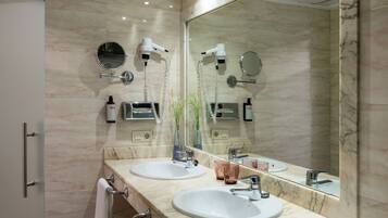 Une salle de bain moderne avec deux lavabos, un grand miroir et des sèche-cheveux fixés au mur.