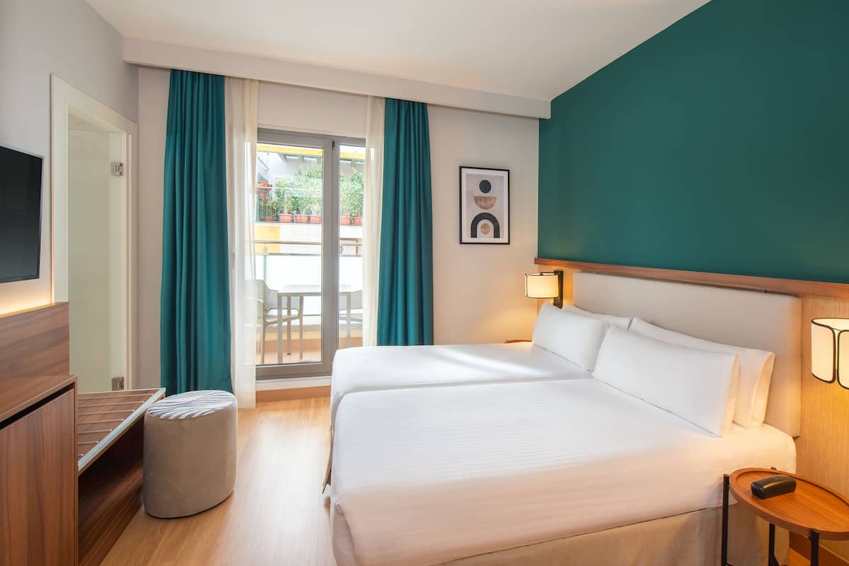 A hotel room with a bed, a TV, a wooden nightstand, and a view of the outdoors through a sliding door.