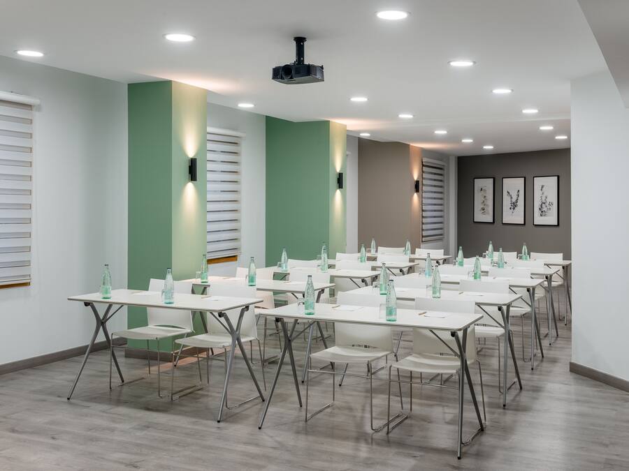 Un salón de conferencias con mesas y sillas, un proyector y cuadros en la pared.
