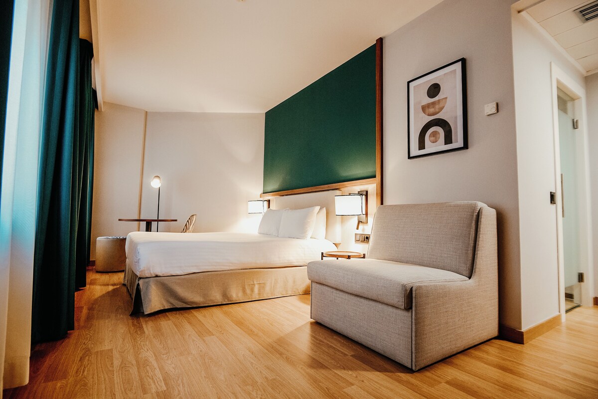 Una habitación de hotel con una cama, una silla, un escritorio y una obra de arte colgada en la pared.
