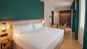 Habitació d'hotel amb un llit gran, abacines, una taula petita amb un comandament a distància i un escriptori de fusta amb una cadira.