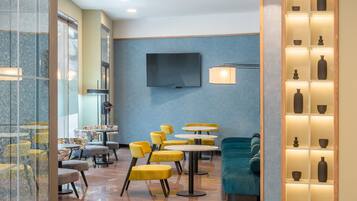 A modern hotel lobby with yellow and blue seating, a flat-screen TV, and a display of decorative vases.