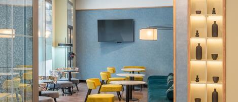 Een moderne hotellobby met geel en blauw zitmeubilair, een flatscreen televisie en een presentatie van decoratieve vazen.