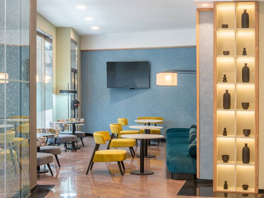 Um saguão de hotel moderno, com assentos em amarelo e azul, uma televisão de tela plana e uma exposição de vasos decorativos.