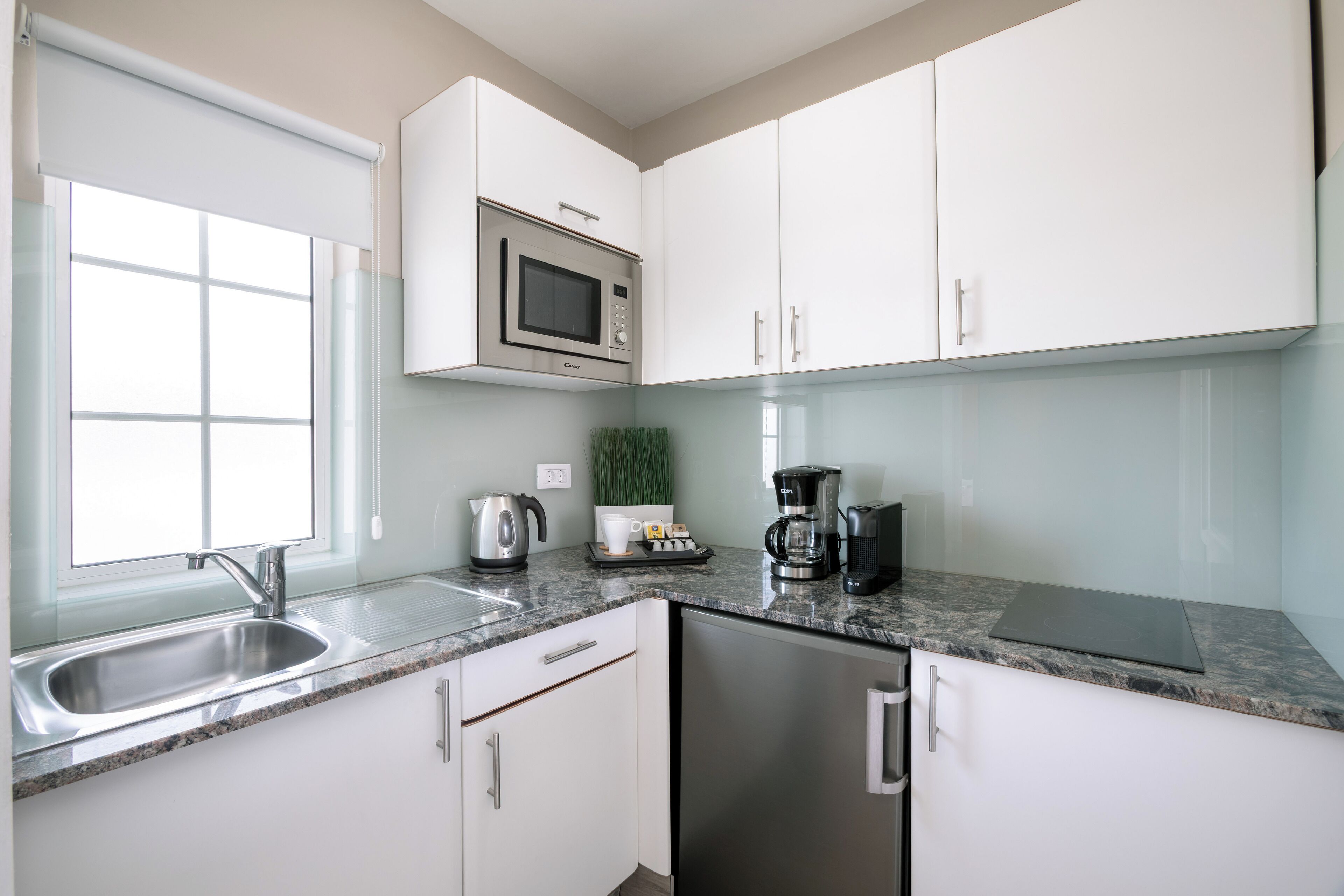 A modern kitchen with white cabinets, a stainless steel sink, a built-in microwave, and a coffee maker.