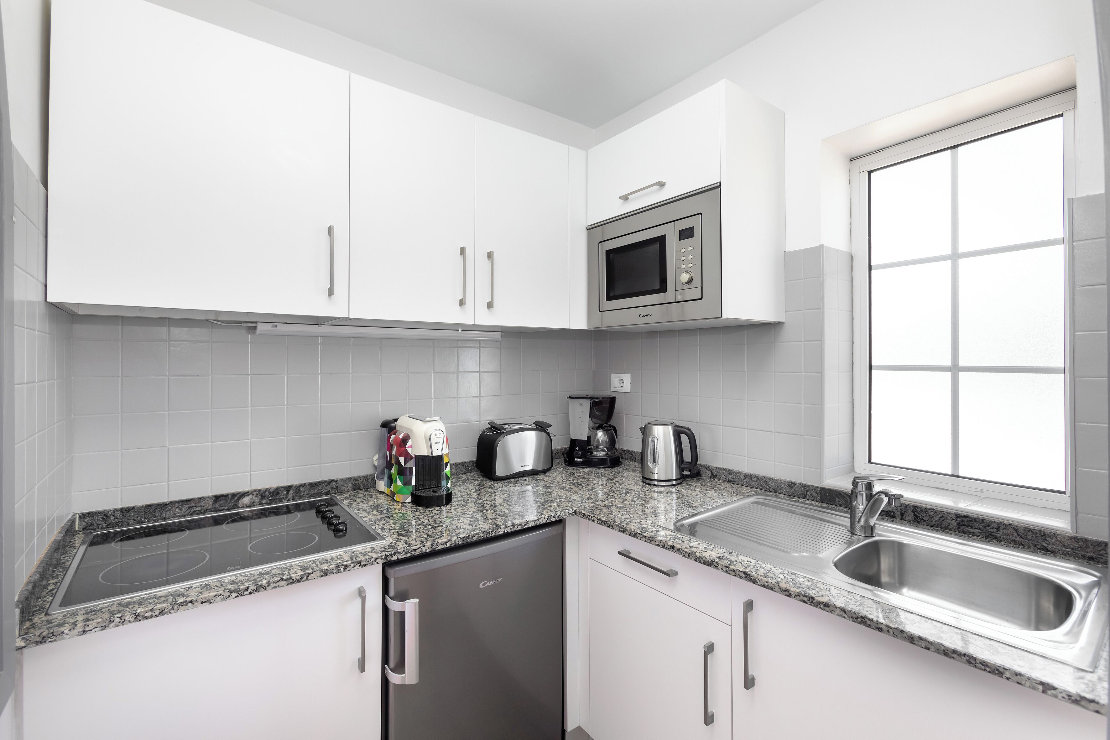 Una cocina moderna con armarios blancos, microondas integrado, cafetera, tostadora y lavavajillas.