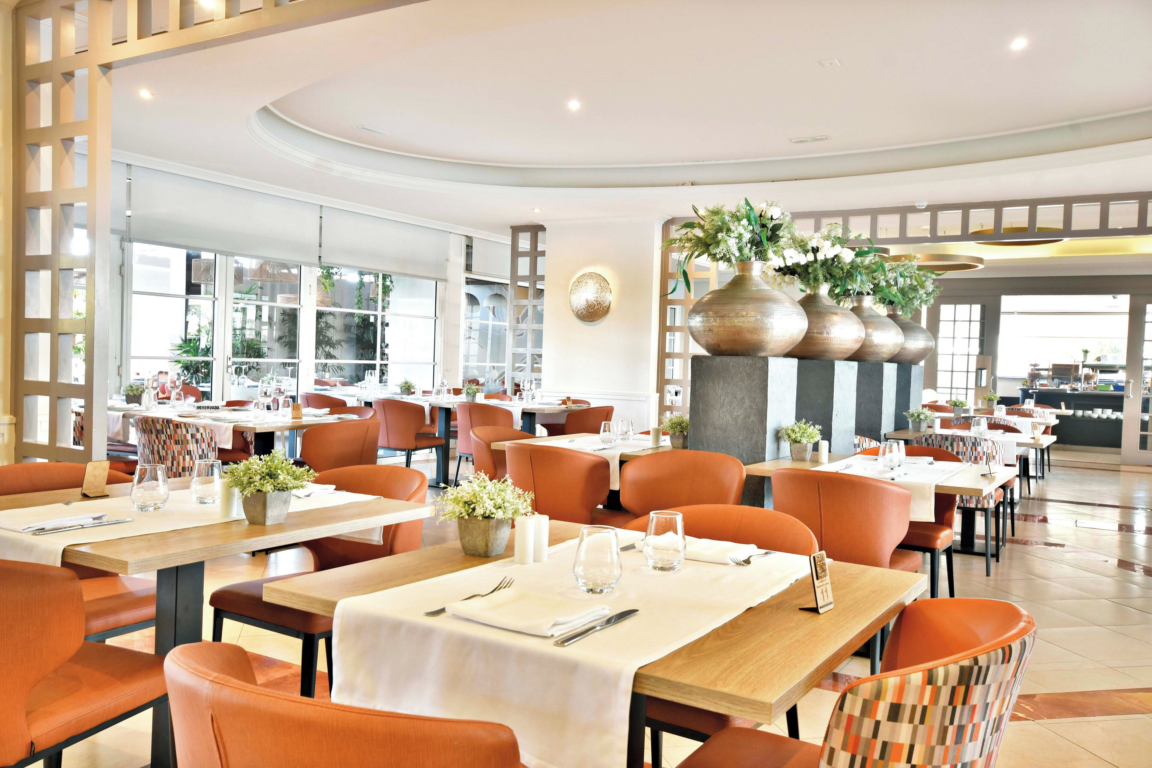 Un restaurant spacieux avec de hauts plafonds, des chaises orange et des tables recouvertes de nappes blanches.