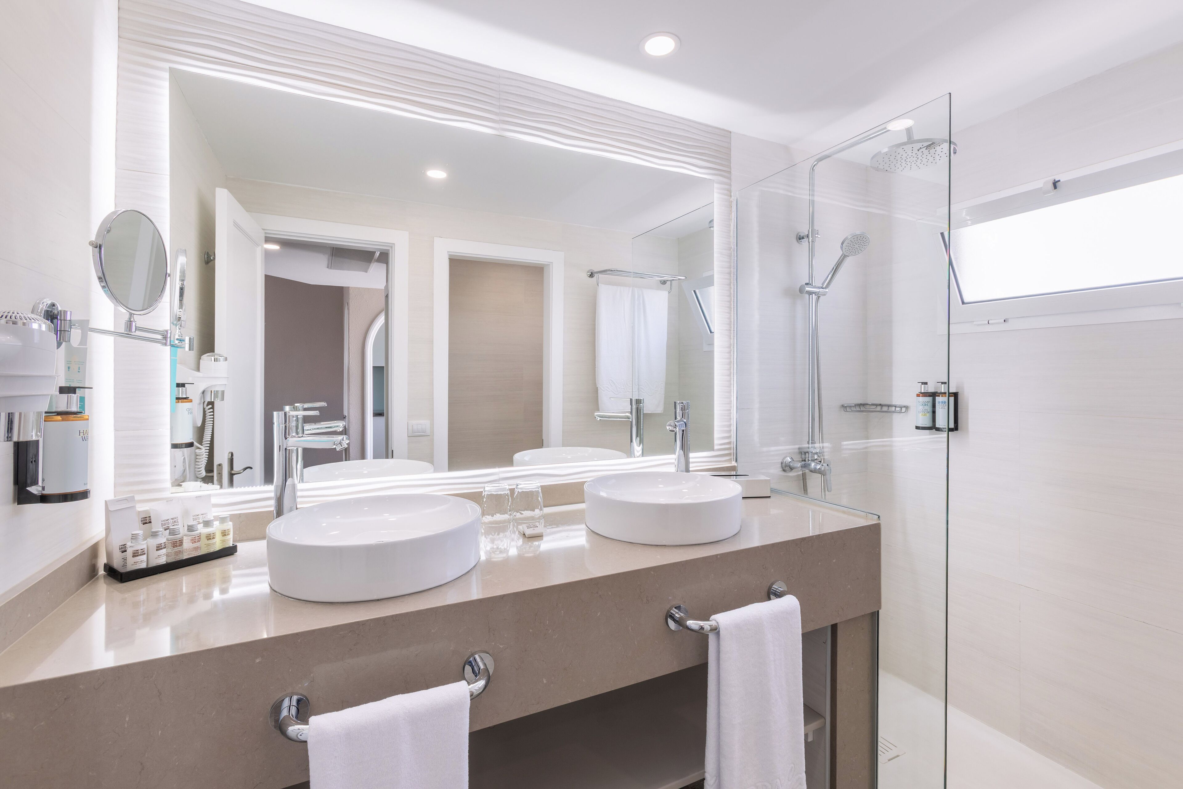 Un baño moderno con dos lavamanos, un espejo grande y una ducha con mampara de vidrio.